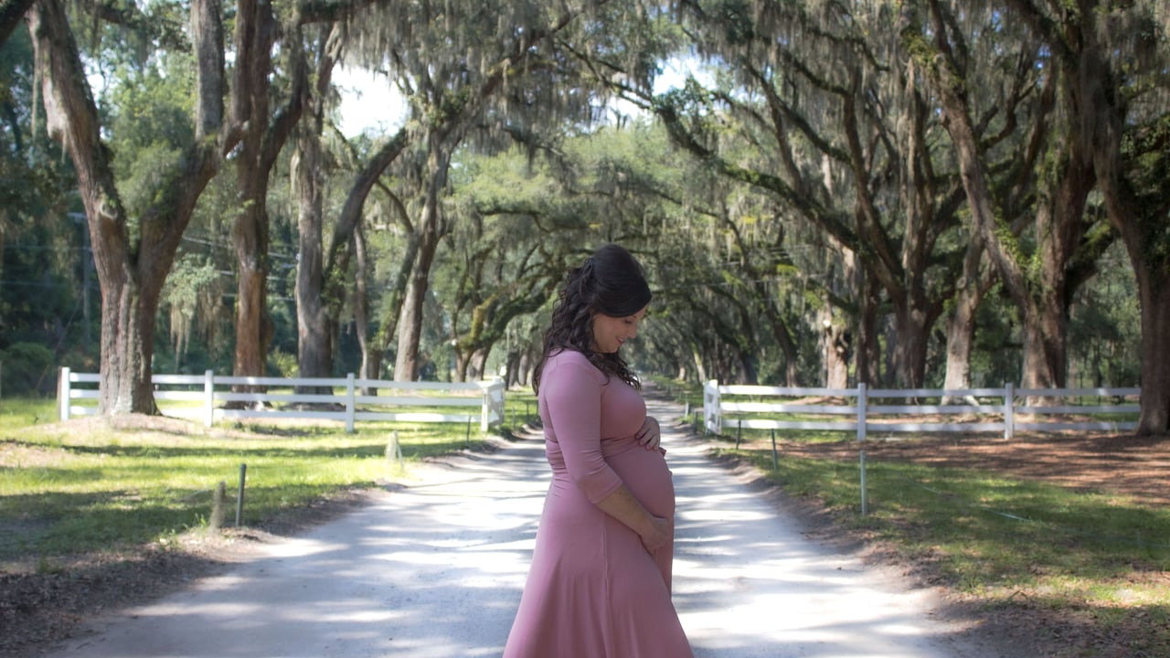 Dr. Nicole walking through a tree-lined driveway, pregnant with her third